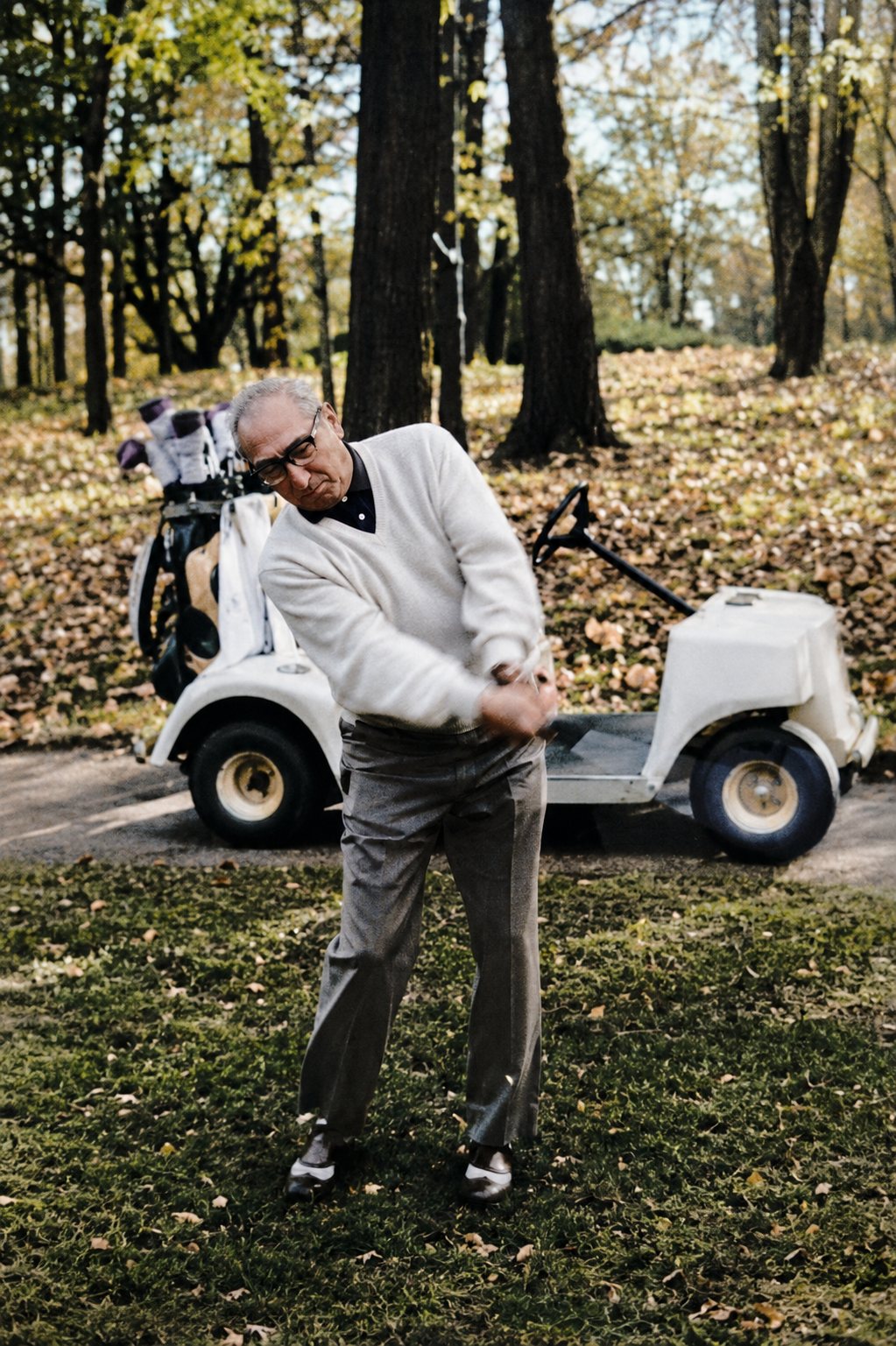 Peter Green swinging a golf club beside a golf cart